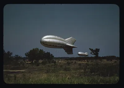 Two silver barrage balloons flying over a grassy field