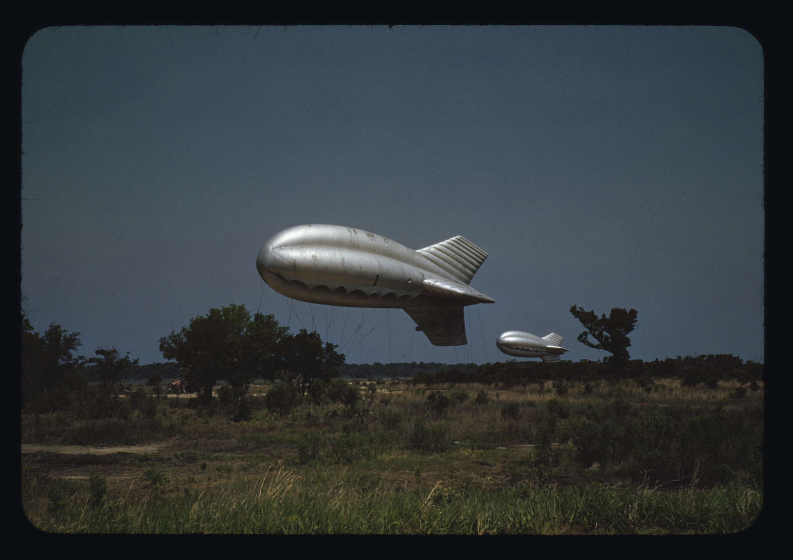 Two silver barrage balloons flying over a grassy field — historic image
