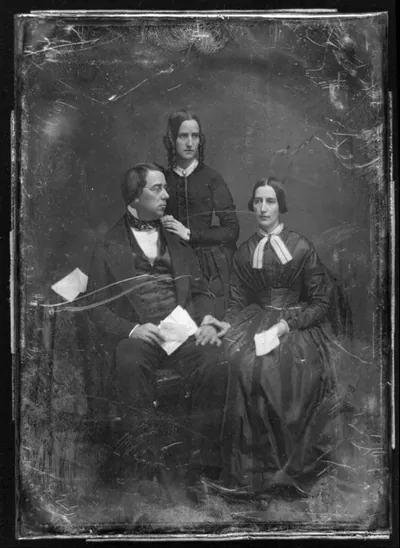 [George Perkins Marsh family. Marsh seated beside a table with tablecloth, on the left, his head turned to the right, wearing spectacles, his wife seated on the right, her hand on his, her head slightly to the left, both holding papers; Caroline's sister, Lucy Crane, standing behind and between them, her hands on her brother-in-law's shoulder, her head three-quarters to the right]