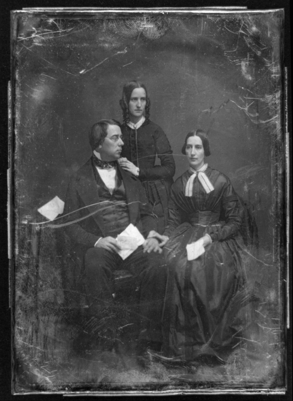 [George Perkins Marsh family. Marsh seated beside a table with tablecloth, on the left, his head turned to the right, wearing spectacles, his wife seated on the right, her hand on his, her head slightly to the left, both holding papers; Caroline's sister, Lucy Crane, standing behind and between them, her hands on her brother-in-law's shoulder, her head three-quarters to the right], [between 1844 and 1849] — historic photograph