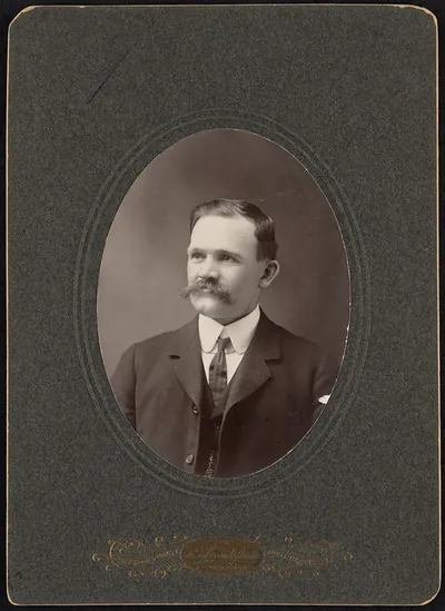 Sepia studio portrait of a mustached man in suit and tie