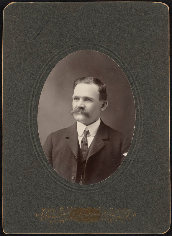 Sepia studio portrait of a mustached man in suit and tie — historic image
