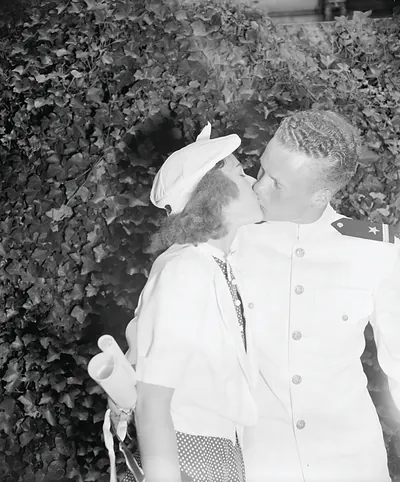 Sailor in white uniform kissing woman before ivy hedge