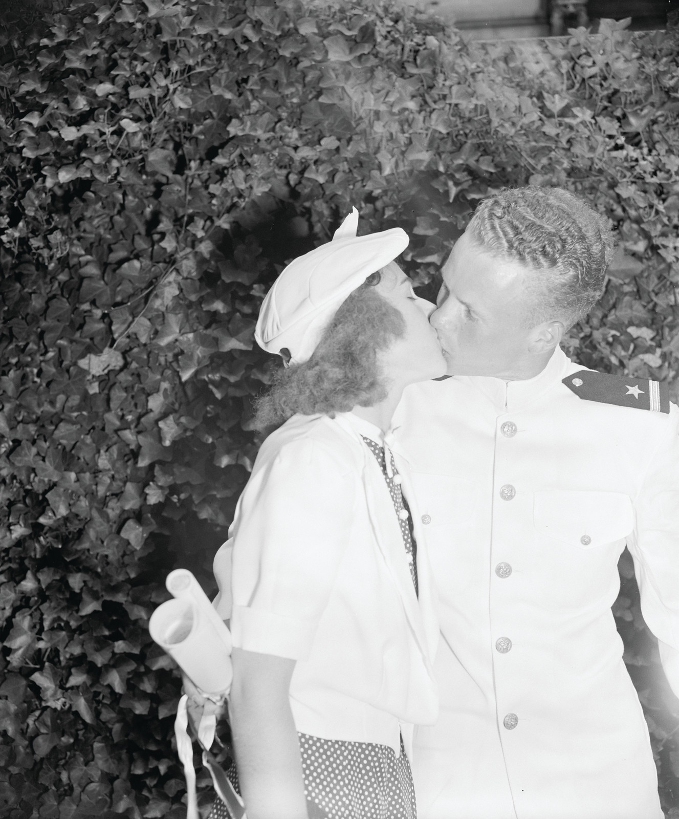 Sailor in white uniform kissing woman before ivy hedge — historic image