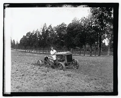 Woman driving tractor plowing a field, early photograph