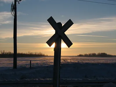 Railroad crossing sign silhouetted at sunset over snowy field
