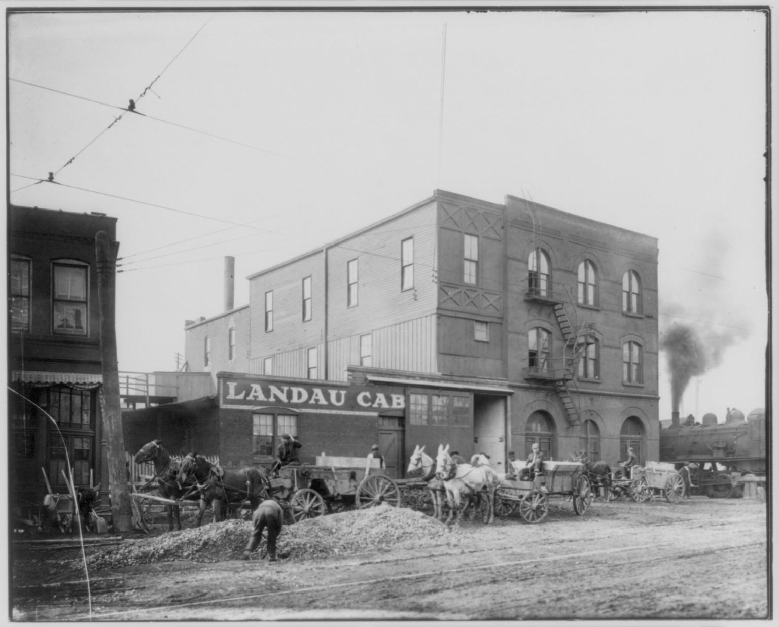 [Horse-drawn wagons in front of Ladau Cab building beside railroad yards, St. Louis, Missouri] — historic photograph