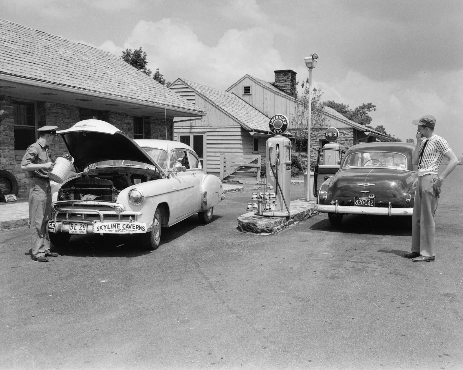 Attendant pouring oil into a white car at a roadside gas station — historic image