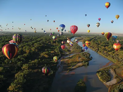 Hot air balloons over a river and cottonwood forest