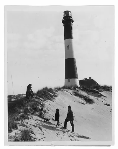 Visitors on sand dunes beside a striped lighthouse station