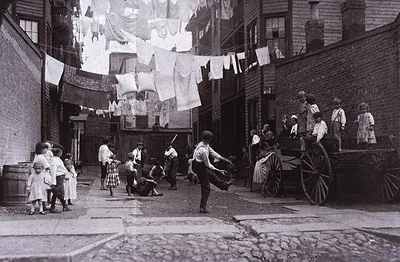 Children playing in a tenement alley under laundry lines