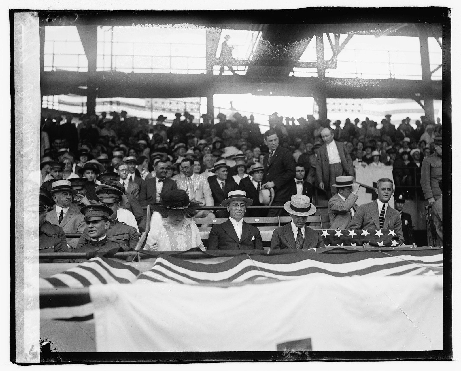 Spectators in a stadium with flag-draped railing and officers — historic image
