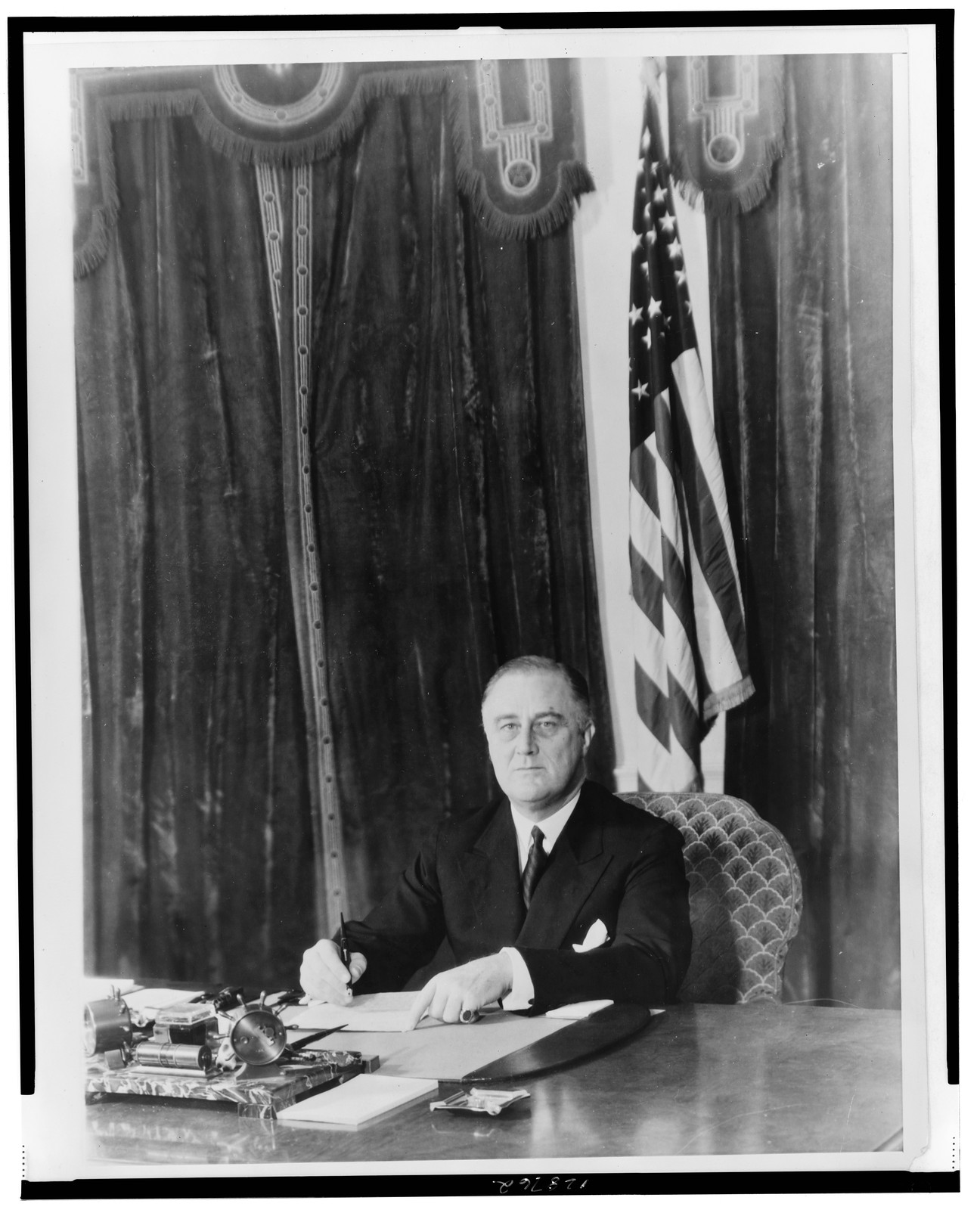 [President Franklin D. Roosevelt, half-length portrait, seated at desk, facing front, signing document], 1935 — historic photograph