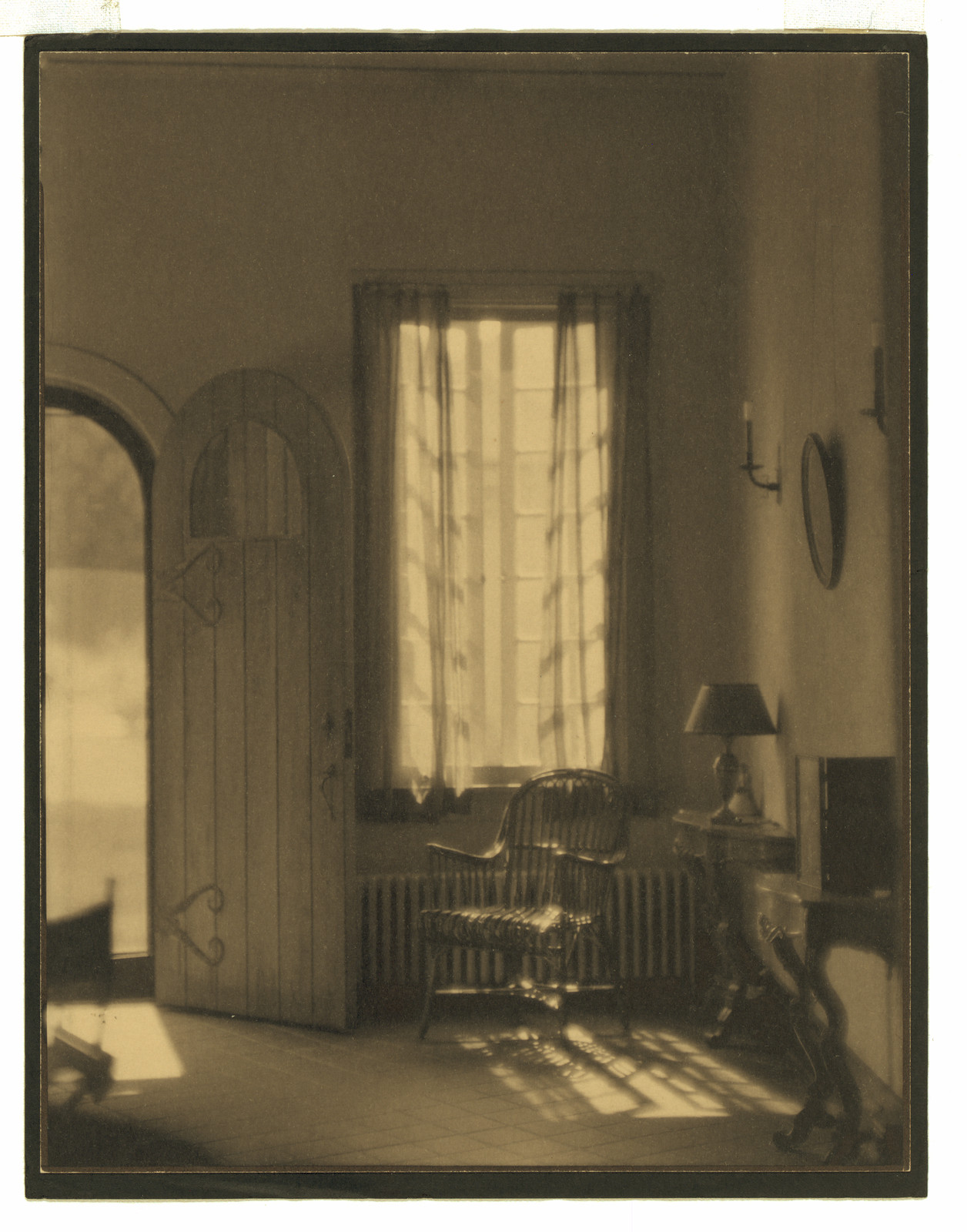 Sunlit interior with arched door and wicker chair — historic image