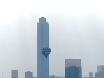 Blue hot air balloon beside a hazy city skyline tower