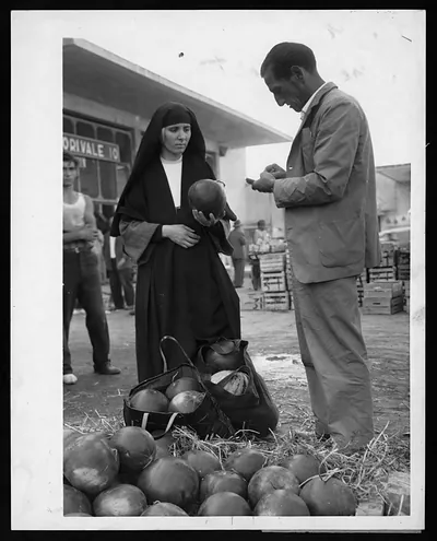 Nun and man inspecting melons at a market