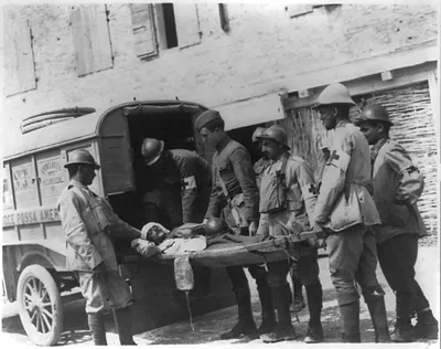[American Red Cross personnel holding wounded soldier on stretcher at rear of ambulance at ambulance advanced post on Piave at the Italian Front during World War I]