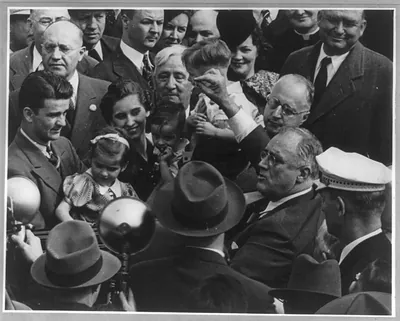 [Franklin Delano Roosevelt, bust, facing left, surrounded by crowd, speaking]