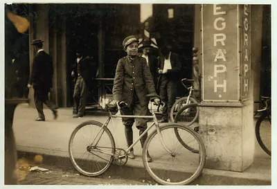 Telegraph messenger boy with bicycle beside street sign