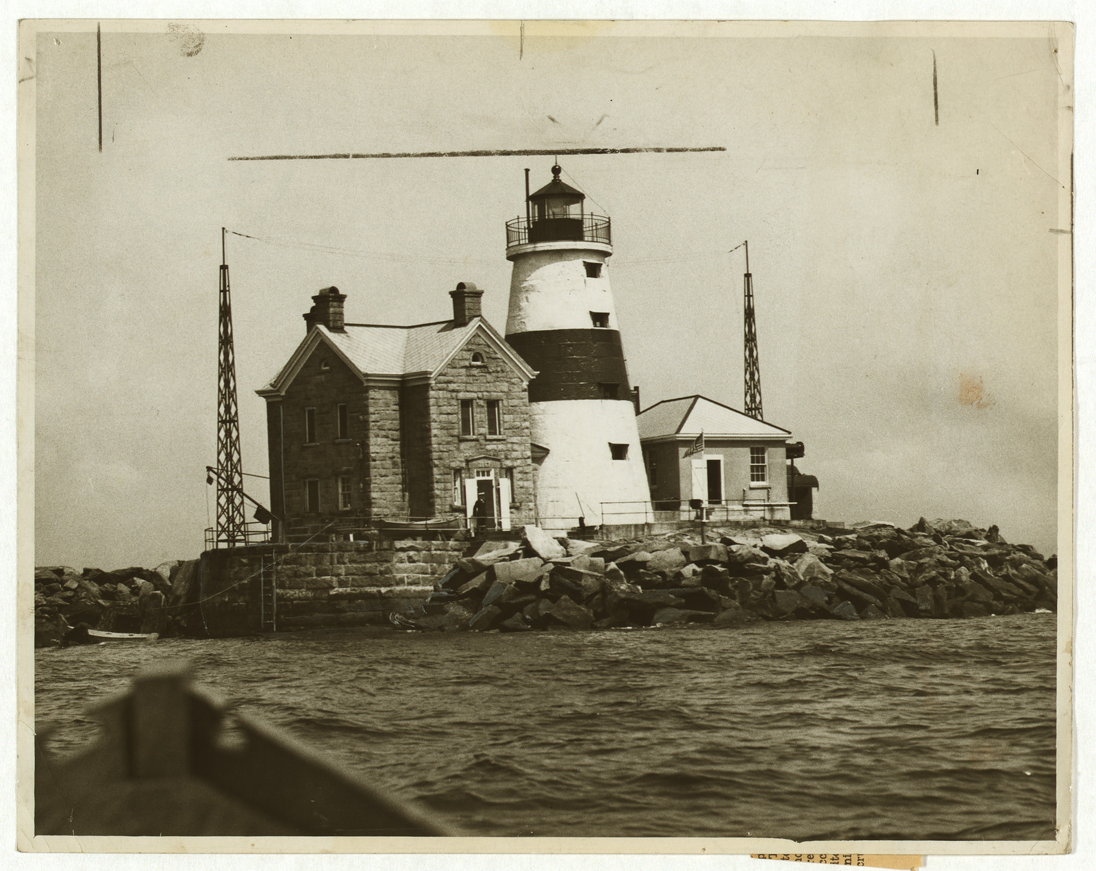 Black and white lighthouse with stone keeper's house on rocks — historic image