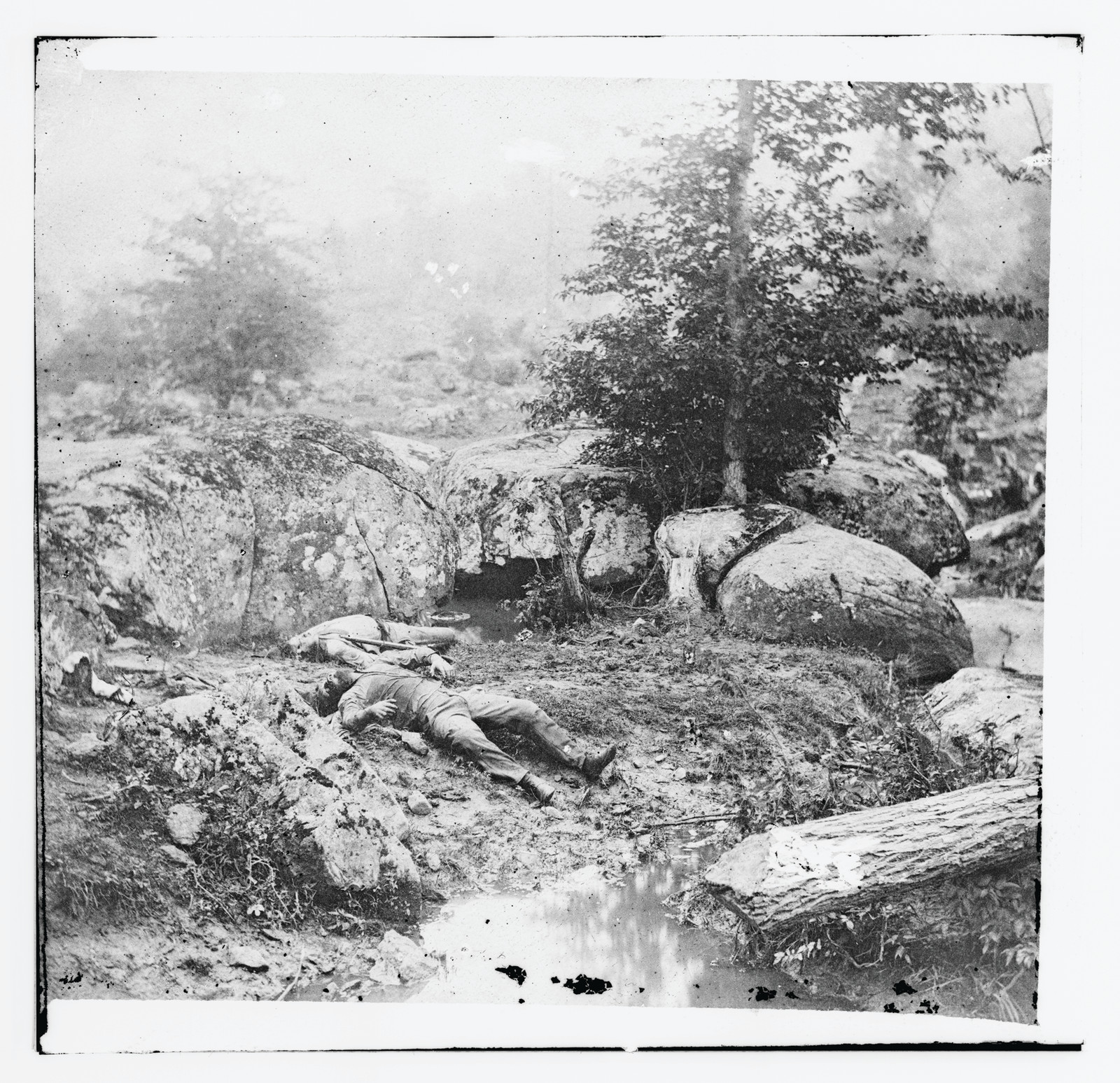 Dead soldiers lying among boulders beside a stream — historic image