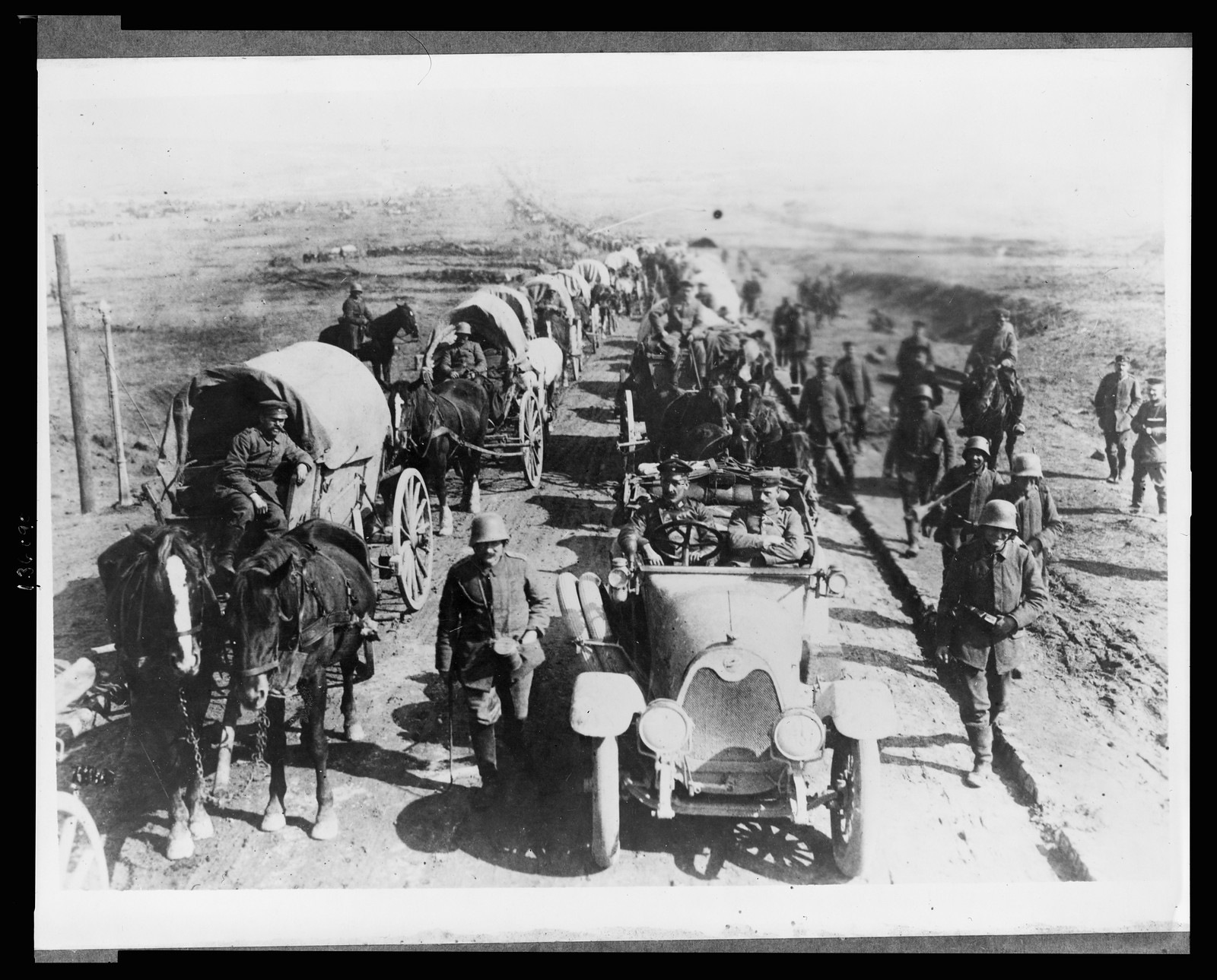 [German officers in an automobile on the road with a convoy of wagons; soldiers walk along side the road], [between 1914 and 1918] — historic photograph