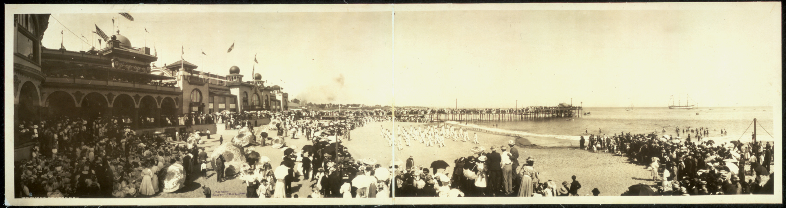 Crowded beach with arcaded pavilion and long pier, sepia panorama — historic image