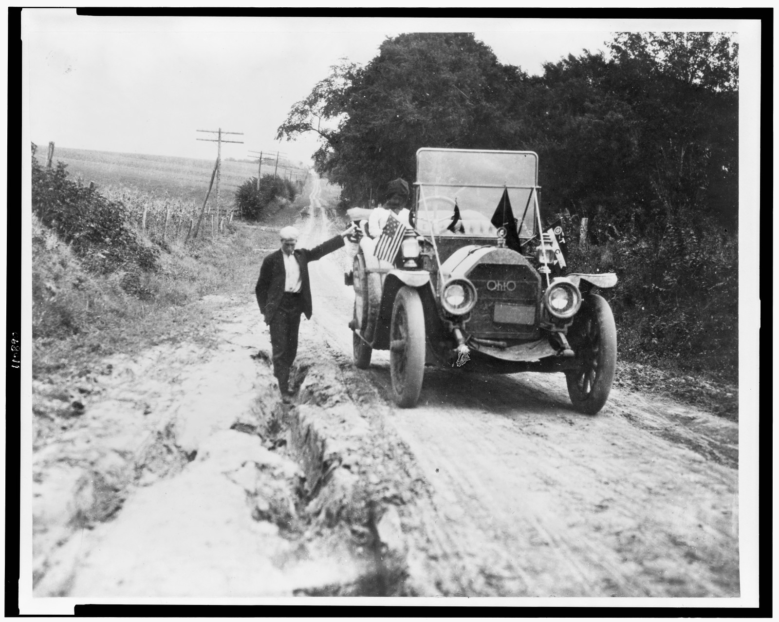 [Man standing in rut, with hand on automobile], [192-(?)] — historic photograph