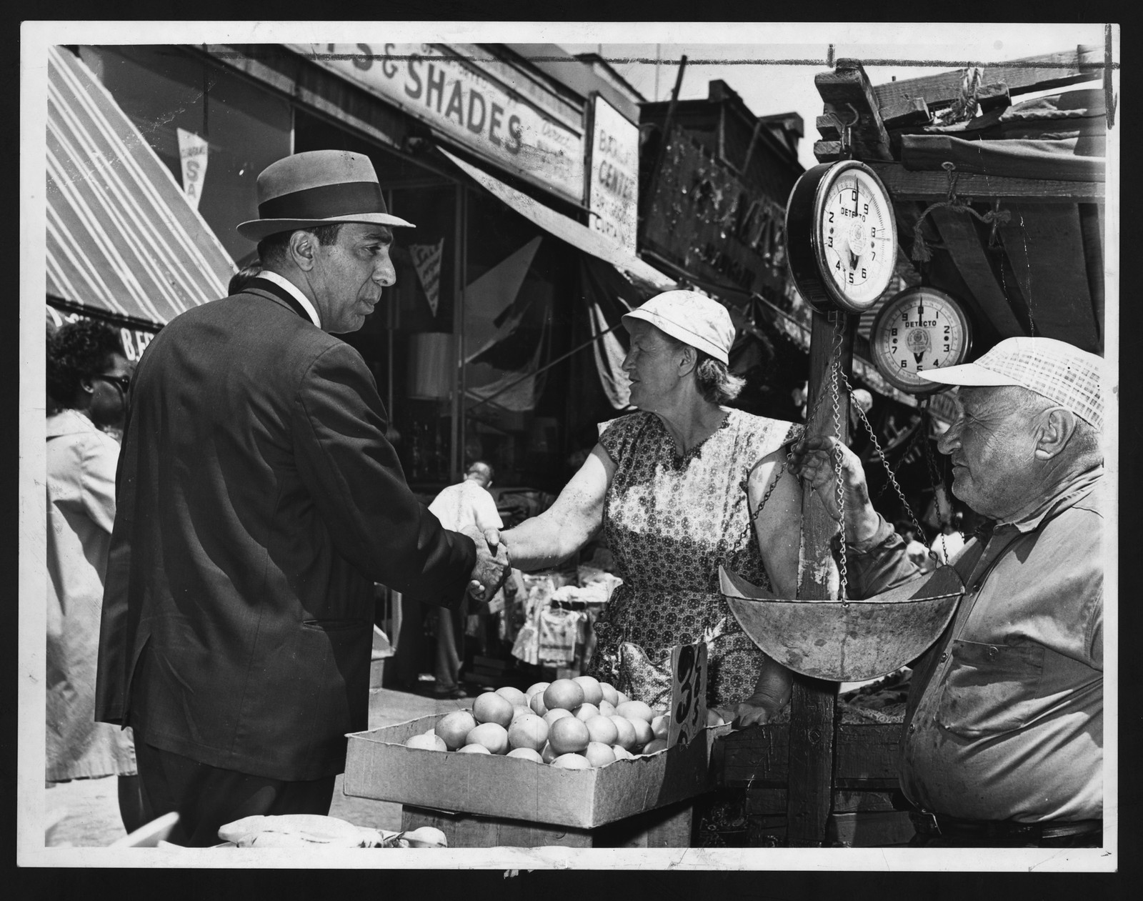 Man in fedora shaking hands with vendor at produce stand — historic image