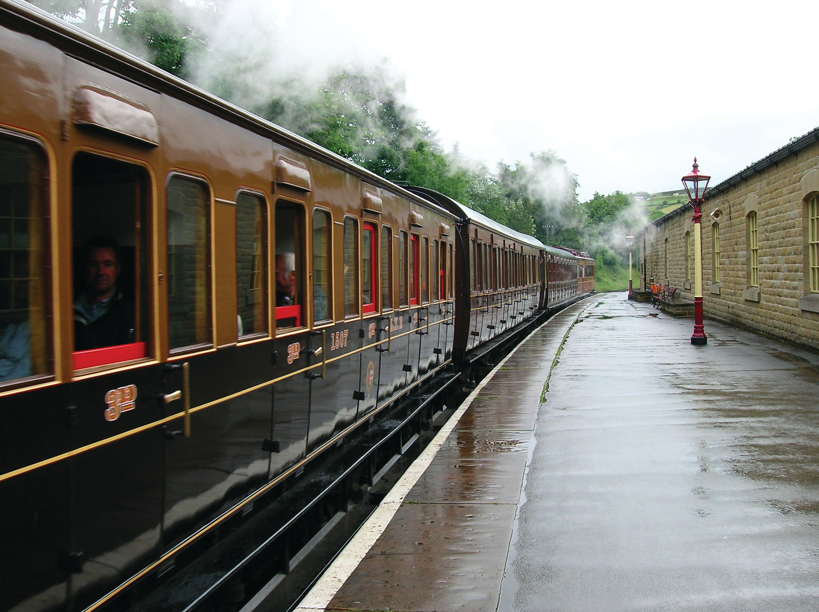 Steam train with brown carriages at a wet stone-station platform — historic image