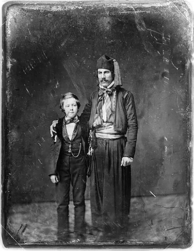 [Unidentified man in Middle Eastern costume with arm around boy, full-length portrait]
