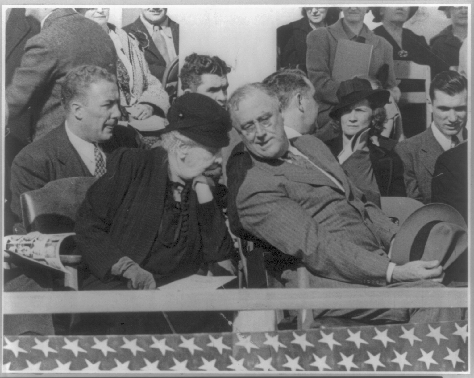 [Franklin Delano Roosevelt, three-quarters length, seated, on reviewing stand, talking to woman beside him] — historic photograph