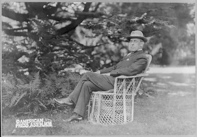 [Woodrow Wilson, full, seated in wicker chair on lawn of Prospect, his home at Princeton, N.J., facing left]