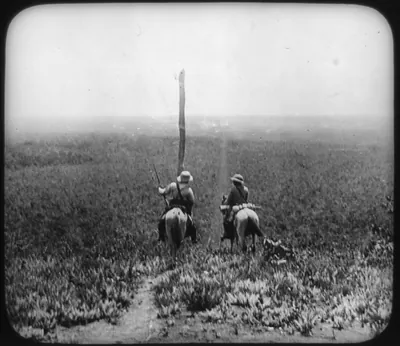 [Rear view of Theodore Roosevelt and another man carrying guns on horses in Africa]