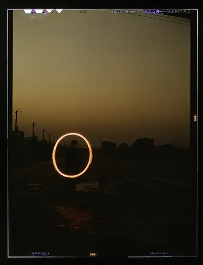 Man swinging a glowing light ring in a railyard at dusk