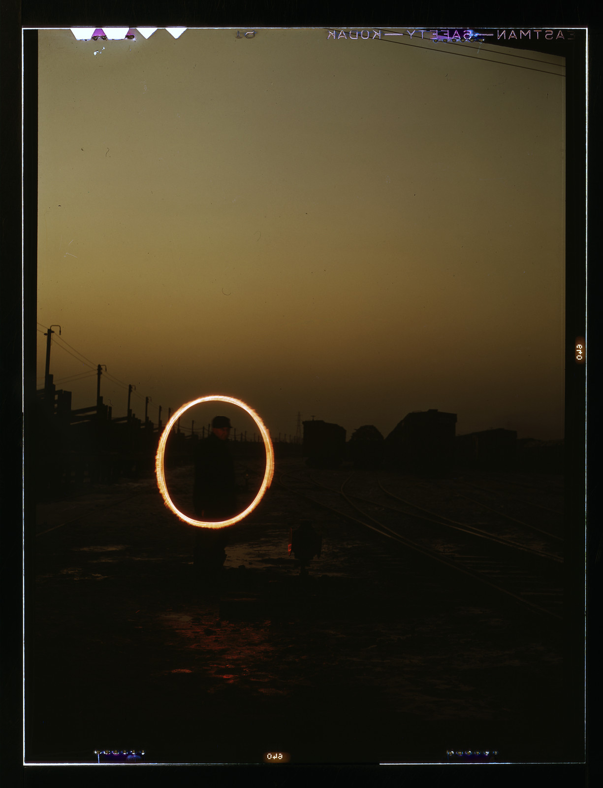 Man swinging a glowing light ring in a railyard at dusk — historic image