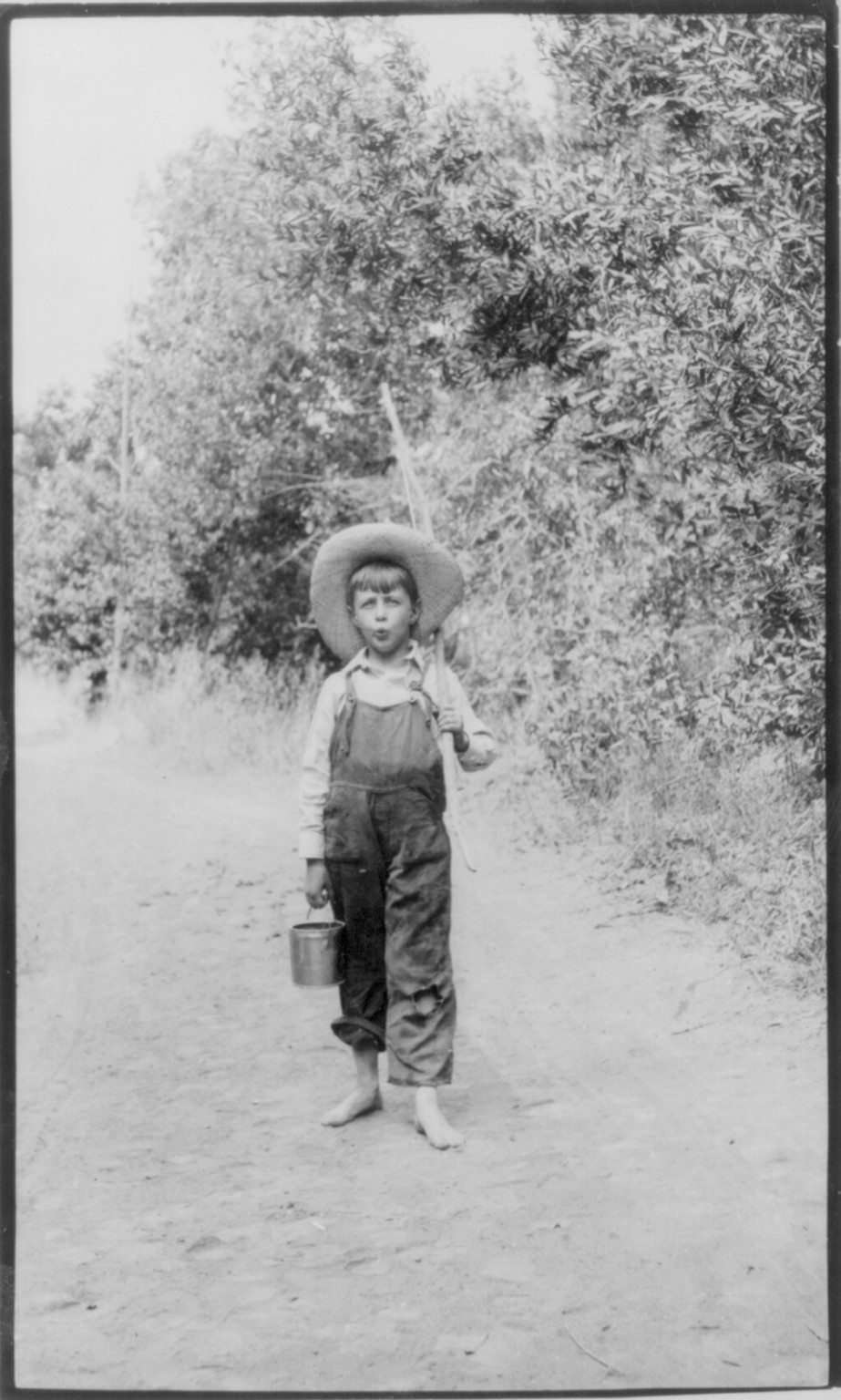 [Rural scenes of children fishing: barefoot boy" on dirt road with wood pole]" — historic photograph