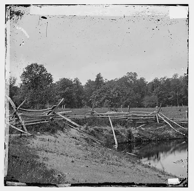 Broken split-rail fence along a creek, trees behind