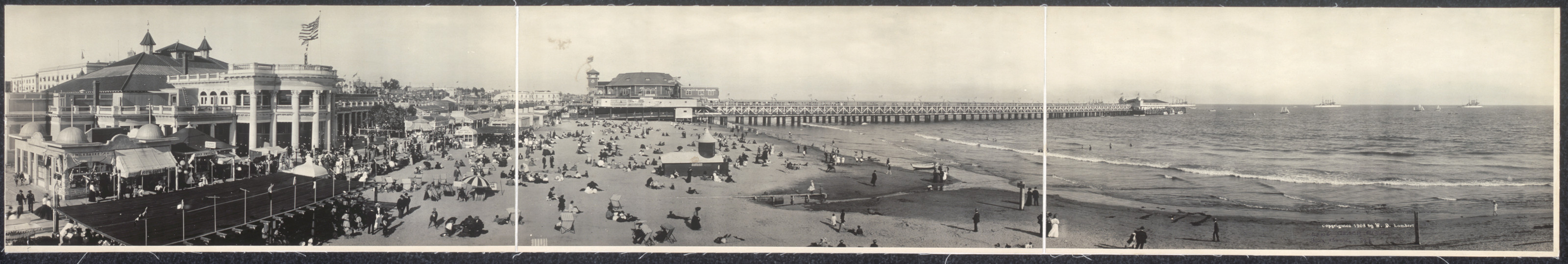 Panoramic photograph of a crowded beach with a long pier — historic photograph