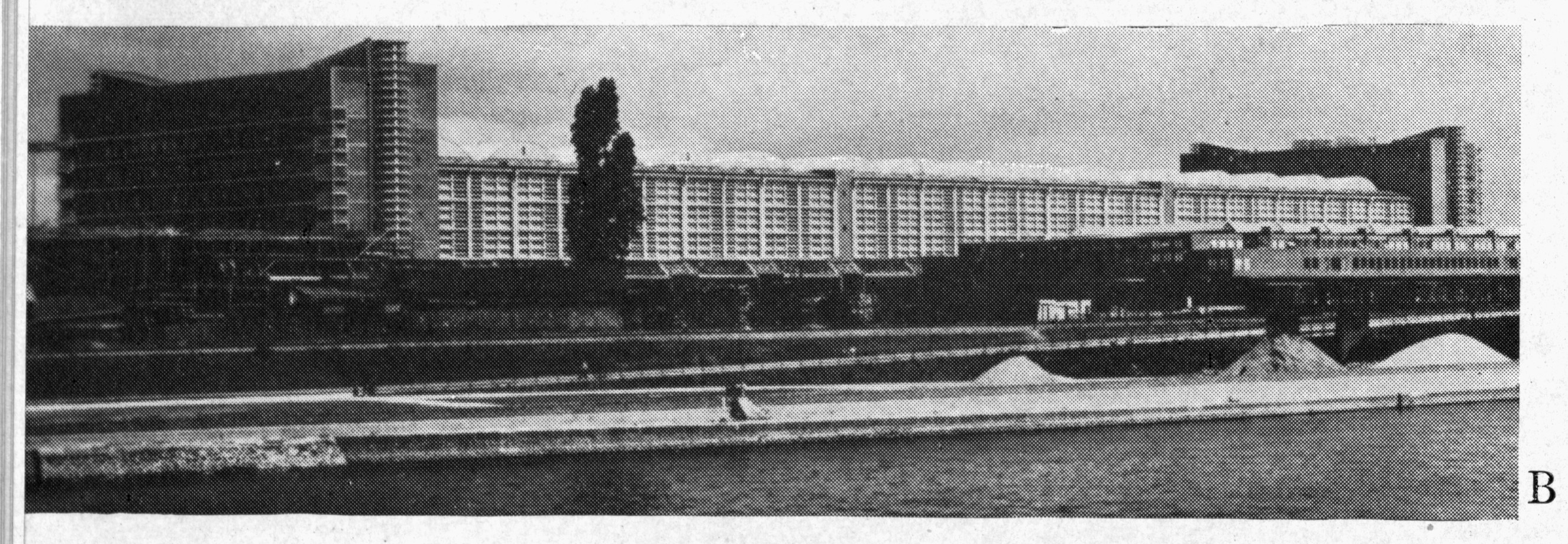 Exterior view of a long market hall beside a river — historic image