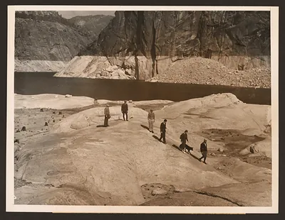 Men with a dog on granite rock above a reservoir