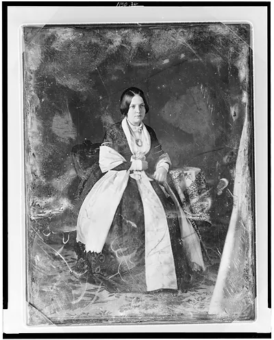 [Unidentified woman, full-length portrait, three-quarter to the right, seated in chair at a small table with tablecloth]