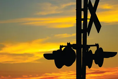 Railroad crossing signal silhouetted against an orange sunset sky