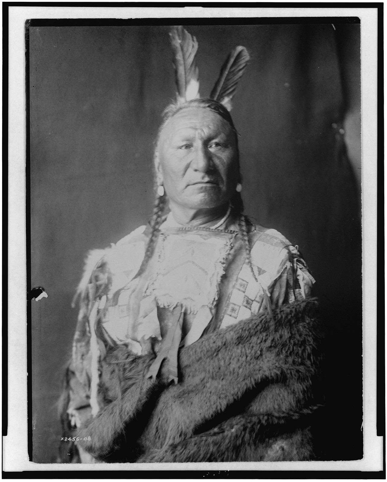 [Yellow Horse--Yanktonai, half-length portrait, standing, facing slightly right, with long braids, two eagle feathers in hair, wrapped in buffalo skin], c1908. — historic photograph