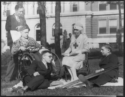 [Grace Goodhue Coolidge, full length portrait, seated in chair on lawn, facing left; as a volunteer Grey Lady of the Red Cross" reading to a group of disabled veterans of the World War [4 men; another man in background] at the Walter Reed Hospital]"