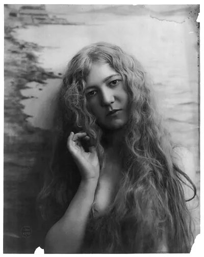 [Young woman modeling: Head and shoulders, with very long hair, right hand raised toward head]