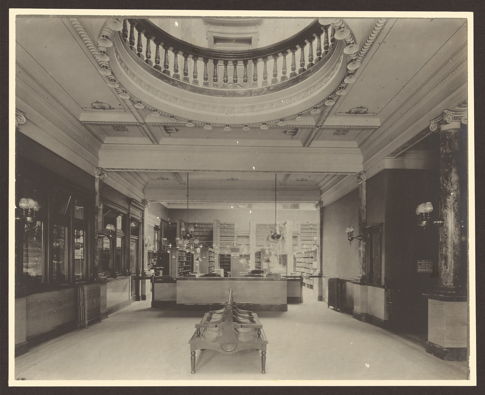 Library circulation desk beneath a balcony with marble columns — historic image