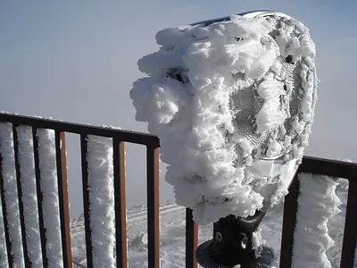 Ice-covered coin-operated viewing telescope on snowy railing