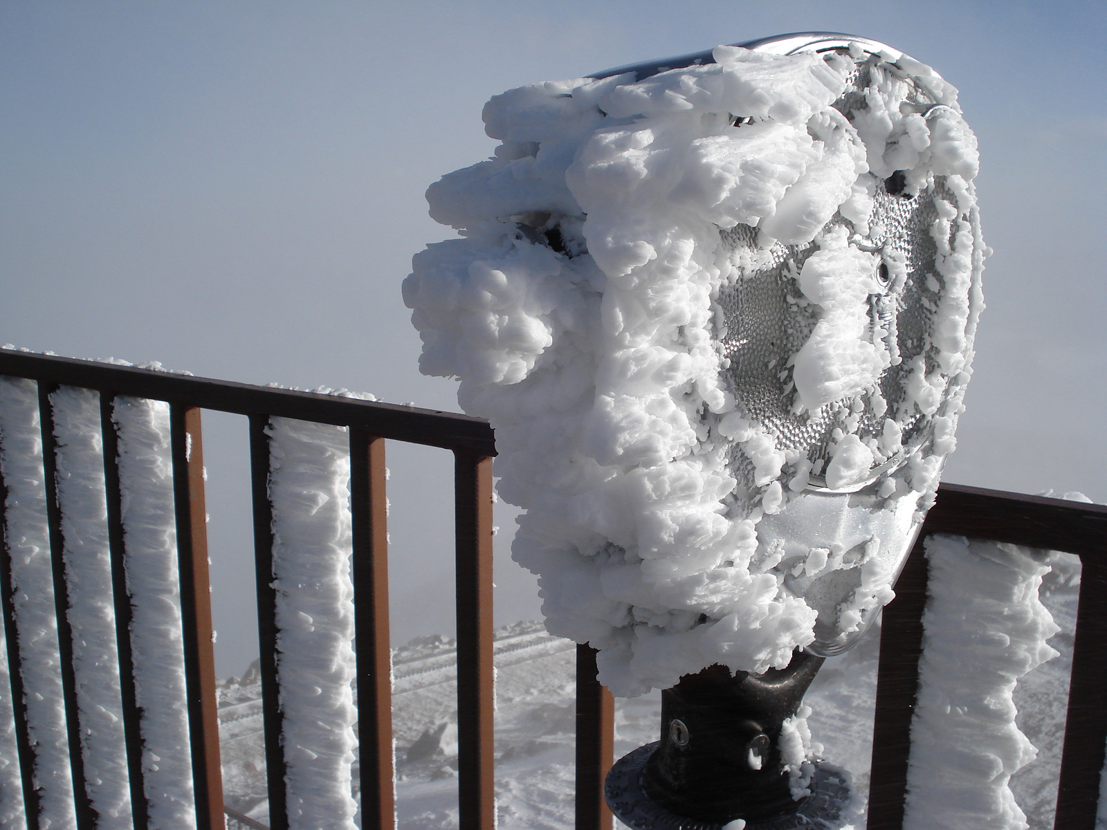 Ice-covered coin-operated viewing telescope on snowy railing — historic image