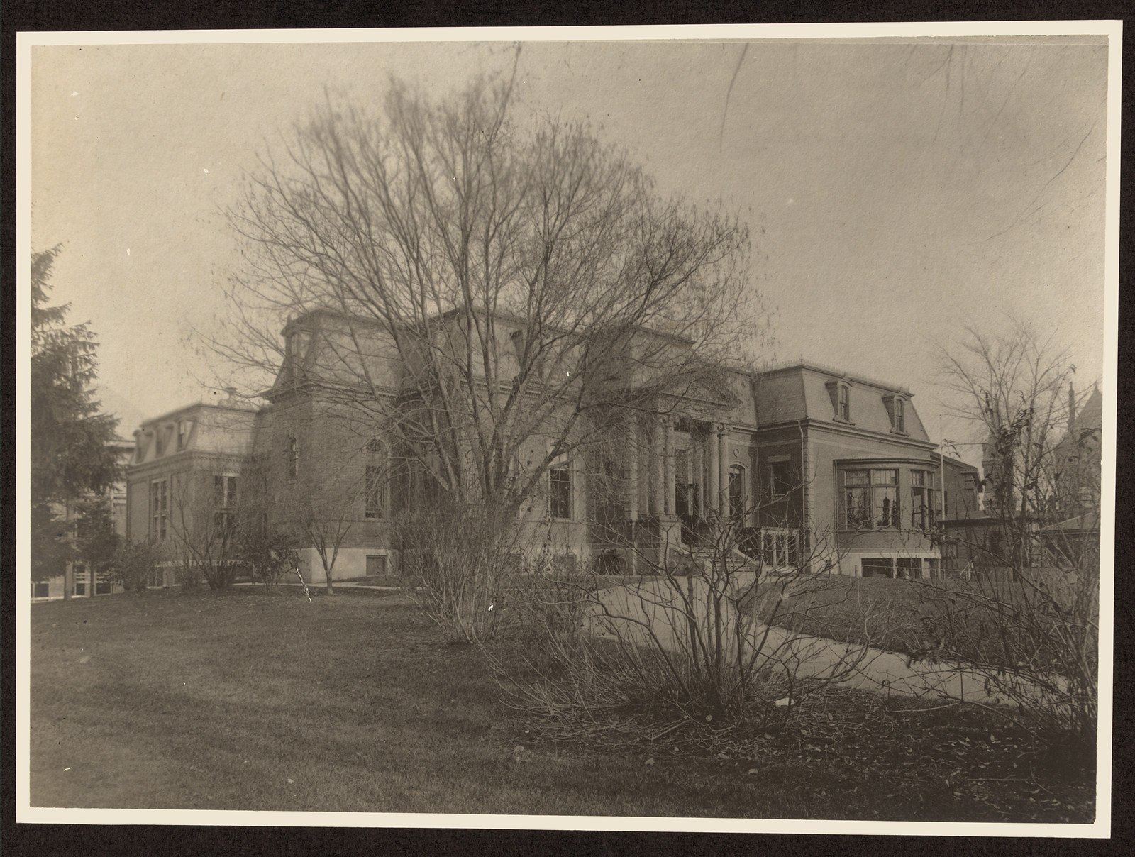 Large classical building with columns, bare trees and lawn — historic image